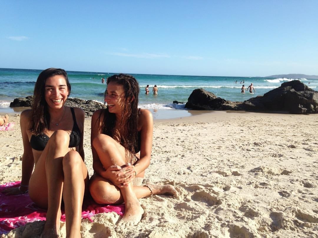 imagen de 2 chicas sentadas en la playa y sonriendo