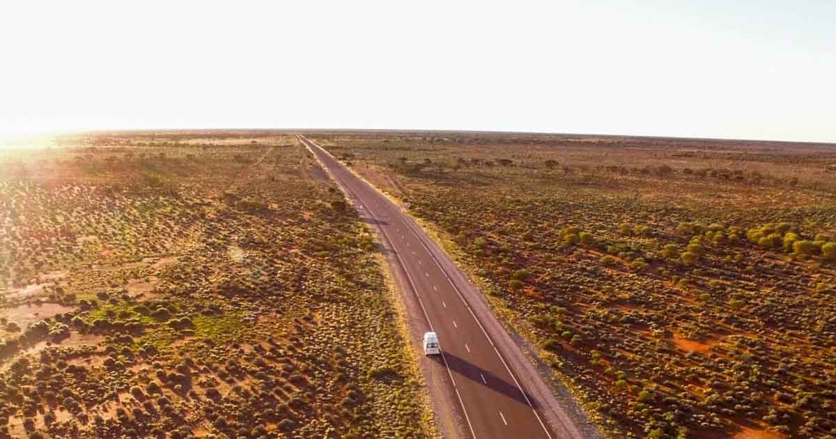 Viajar uluru australia fotografía aérea de una carretera con una caravana y la puesta de sol