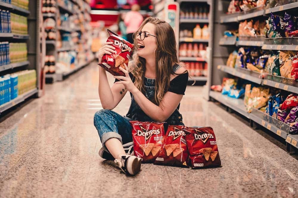 coste de vivir en Nueva Zelanda chica sentada en el suelo de un supermercado con bolsas de Doritos