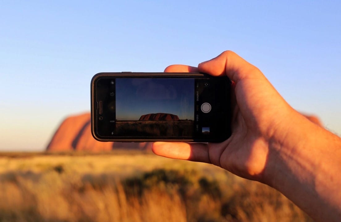 Ser universitario en Sídney Mano sujetando un teléfono que hace fotografía al uluru de Australia