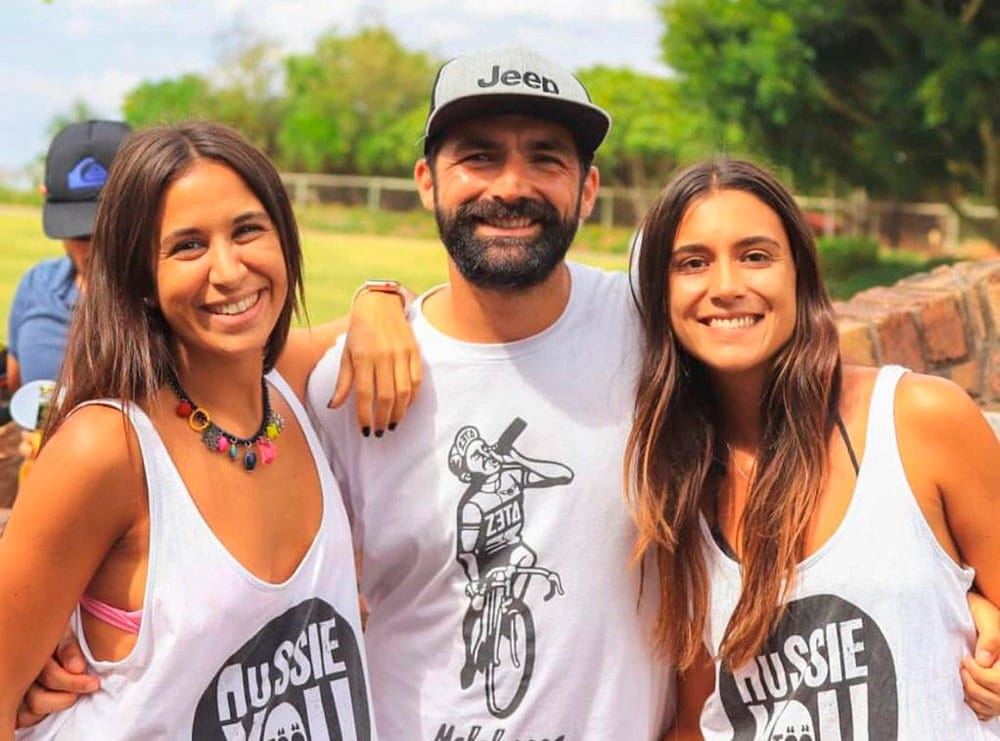 un chico y dos chicas morenos sonriendo a cámara con la camiseta de AUssieYouTOO