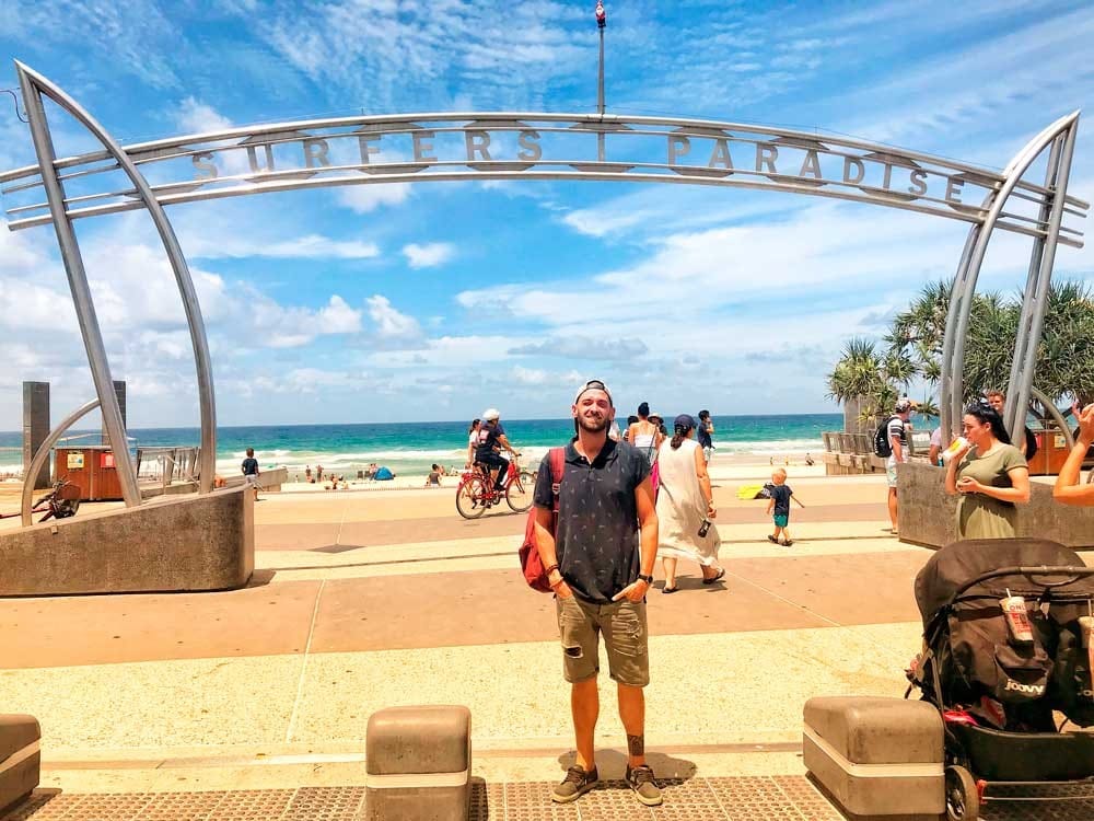 estudiante Gold Coast chico moreno posando delante del paseo marítimo de una playa