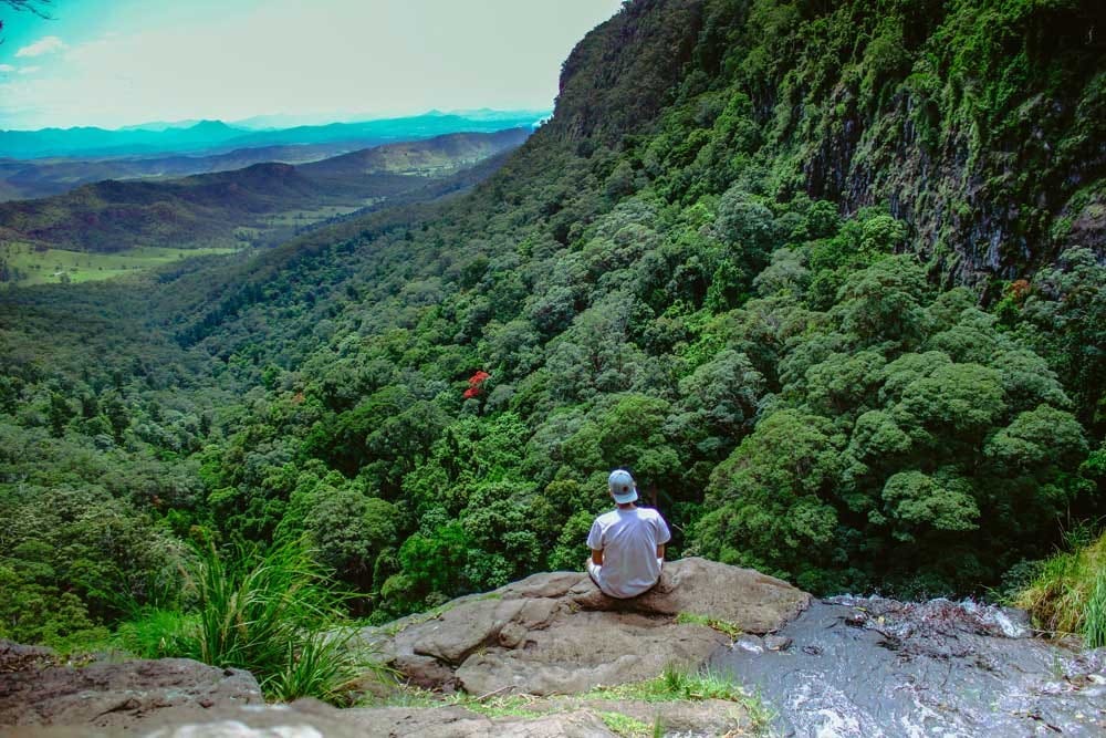 Vivir en Australia chico de espaldas mirando a un paisaje natural muy verdoso