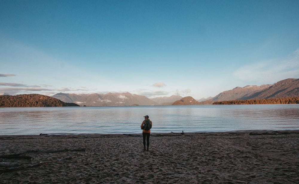 trabajar en nueva zelanda chico de espaldas en la orilla de un lago y delante montañas