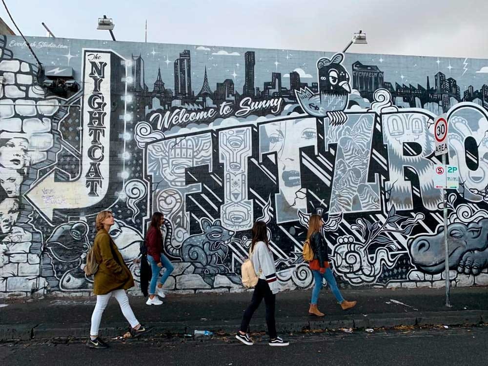 cuatro chicas andando de perfil y detrás tienen una pared con graffities