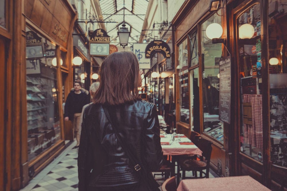 qué necesito para trabajar en Canadá chica morena de espaldas con una chaqueta negra andando por un centro comercial y mirando el escaparate de un restaurante